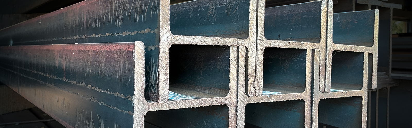 Stacked steel H-beams in a warehouse with the web and flanges visible end-on