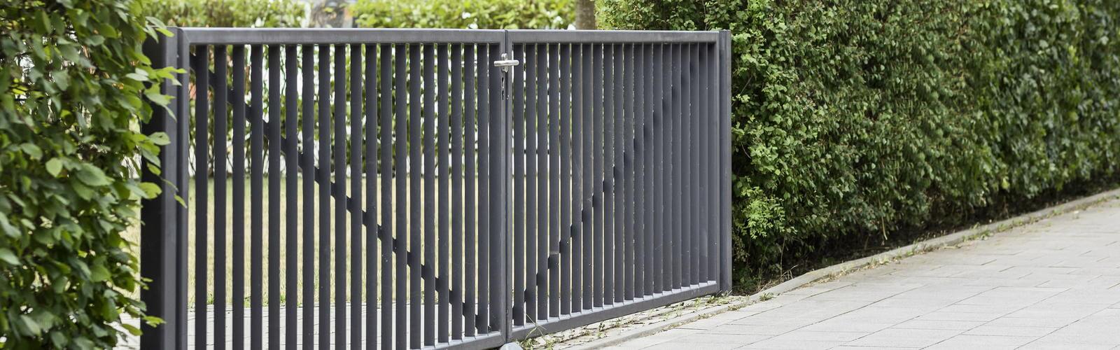 Dark grey powder coated steel garden gate hung between hedges beside a paved path