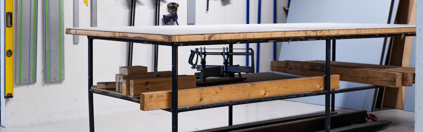 Workbench with a black steel frame, timber top and lower shelf in a home workshop